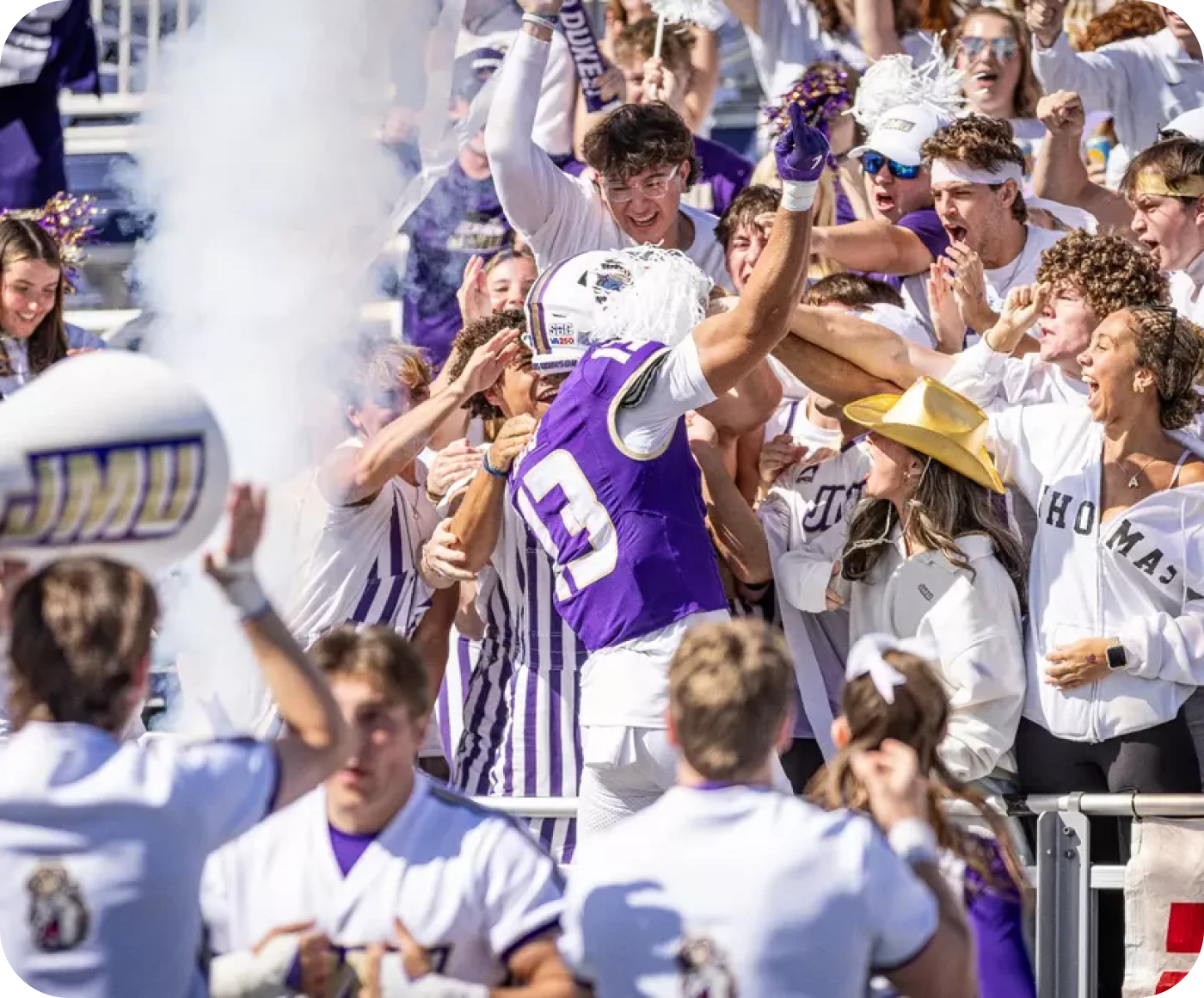 JMU football player celebrating with fans in the stands during a Dukes game